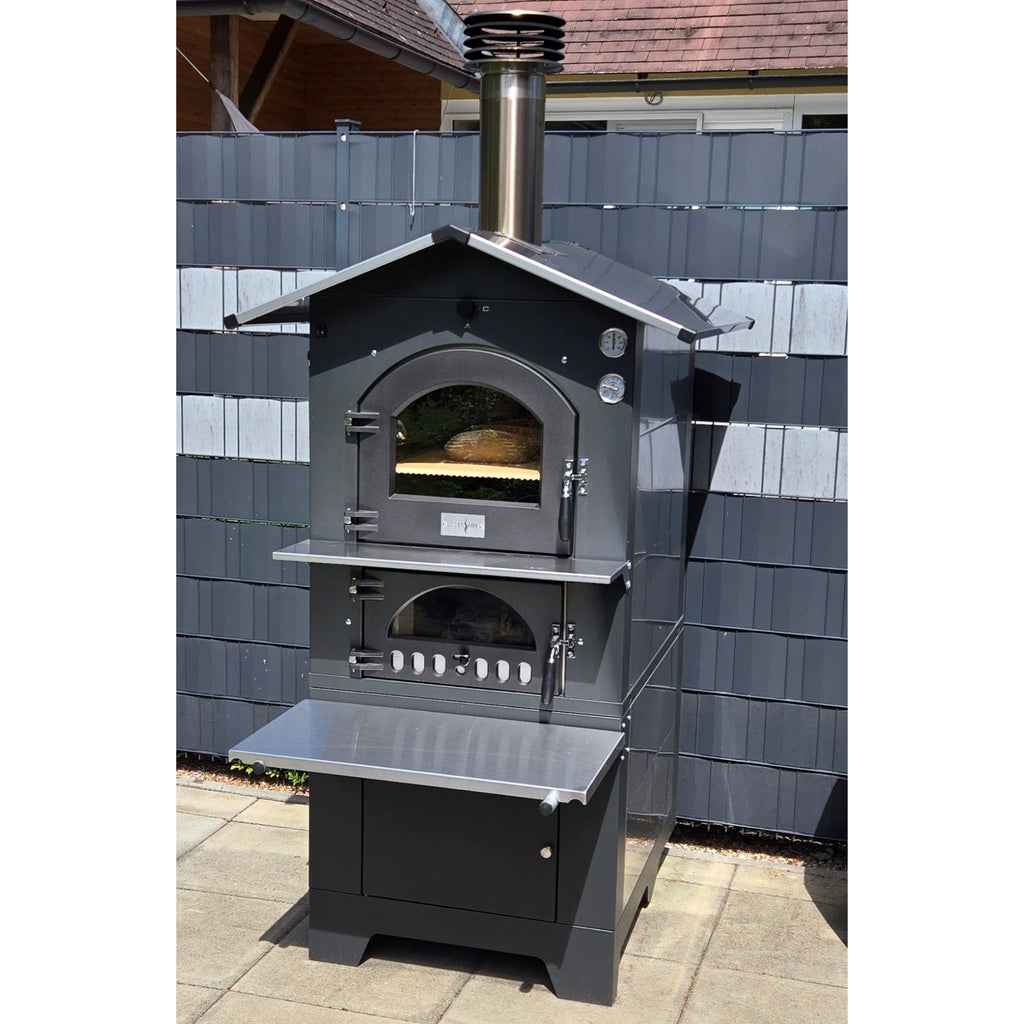 Holzbackofen Gusto Fontana 80x45 freistehend im Garten platziert vor einem klassischen Gartenzaun, ideal für den Außenbereich.